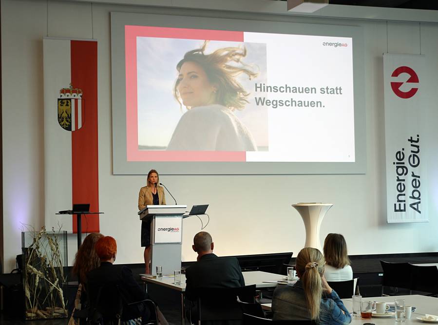 Frau spricht vor Publikum, Präsentationsfolie mit Schriftzug: Hinschauen statt Wegschauen
